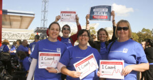 Northcott staff and federal member for Parramatta Julie Owens wearing blue shirts, smiling and holding signs that say "Make it Real" and promote an NDIS