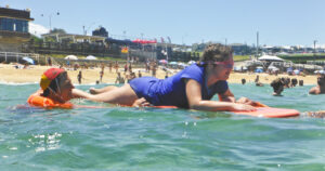 girl learning how to surf, lying down on a surfboard in the ocean