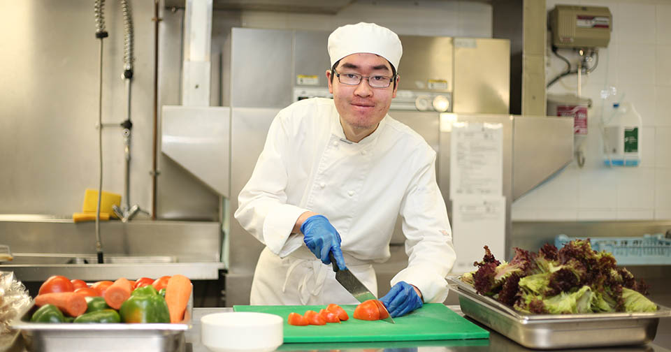 Northcott casula customer Henry cutting vegetables in his chef uniform
