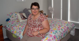 Northcott customer Kelly smiling sitting on her bed