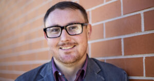 Man with glasses and short dark hair smiles at camera