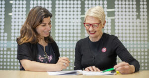 Two women sitting at a table and smiling while looking at a document