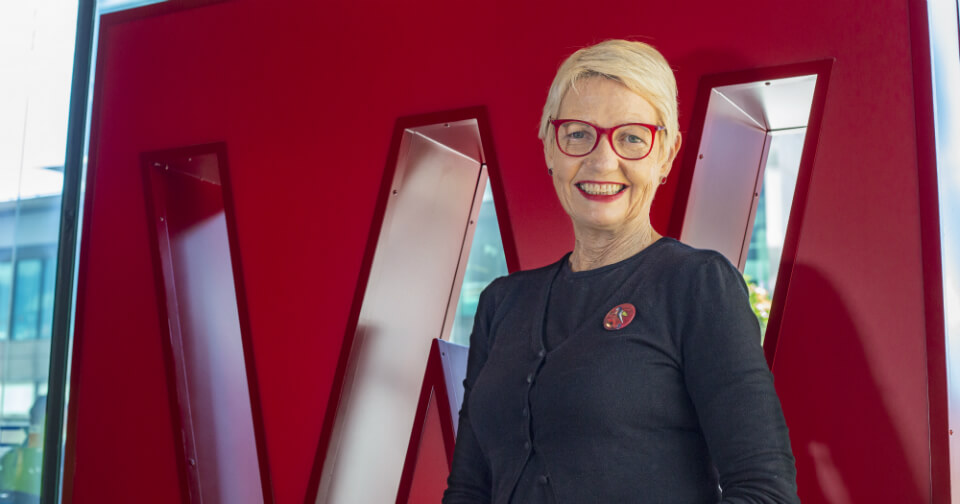 Woman with short blonde hair and red glasses smiles at camera