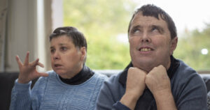 A blind and deaf man sitting on the couch with his housemate