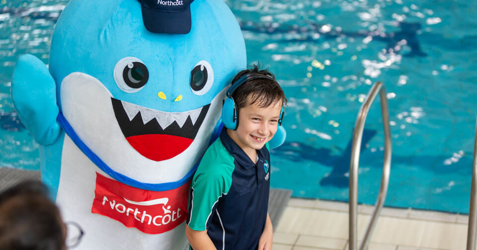 Young child with disability wearing headphones at swimming carnival