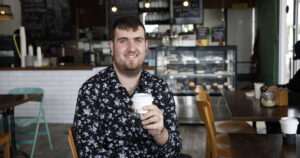 Northcott customer Ben sitting in a café, smiling and holding a coffee