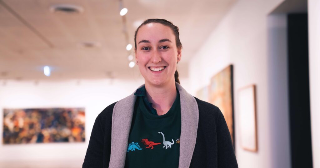 Profile image of young woman with hair pulled back smiling at camera in an indoor setting.