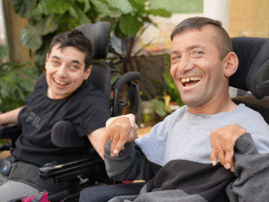 Two adults in power wheelchair smiling in the garden