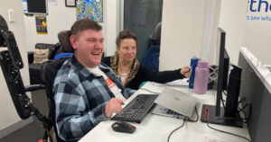 Male in wheelchair behind a desk laughing with female