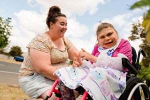 Young girl in wheelchair smiling at camera with woman beside her