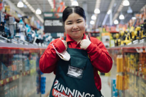 Young female smiling at the camera with her thumbs up in a bunnings apron