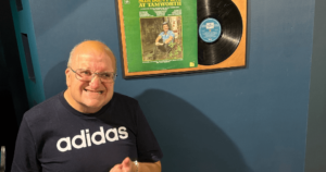 Male smiling standing in front of a blue wall with a record on it