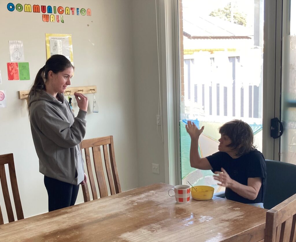 Woman making hand gesture to other woman in living room.