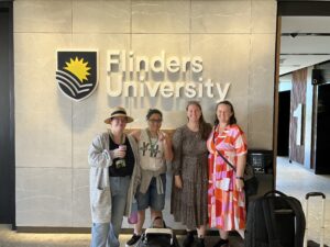 Four women smiling and standing in front of a wall that says Flinders University.