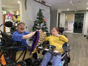 Two people sitting in wheelchairs holding a quilt.