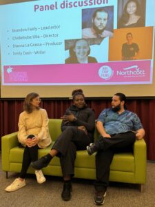 Three adults sitting on a green couch in front of a slideshow presentation.