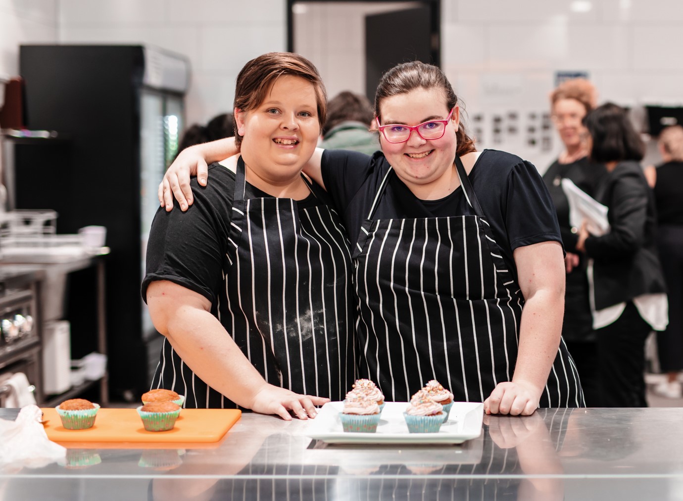 Two teenagers standing in the kitchen in front of cupcakes