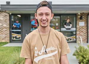 A young smiling man wearing a baseball cap standing in front of a Northcott office