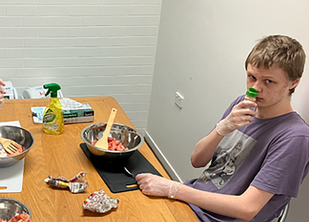 A young man is sniffing a bottle of herbs at a cooking group for people with disability
