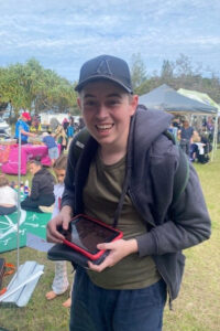 A young man is smiling and holding a small electronic tablet