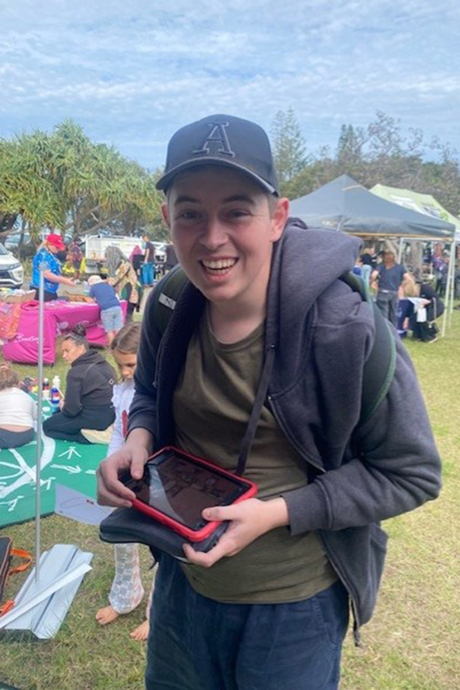 A young man is smiling and holding a small electronic tablet