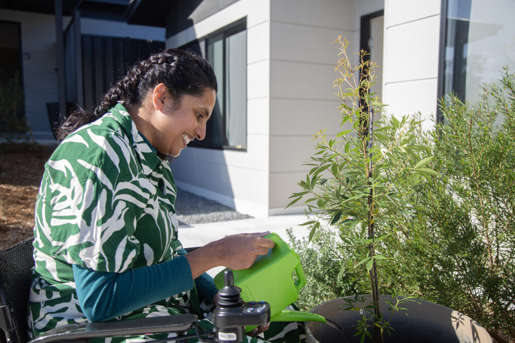 Vindya is watering some plants in her garden with a green watering can.