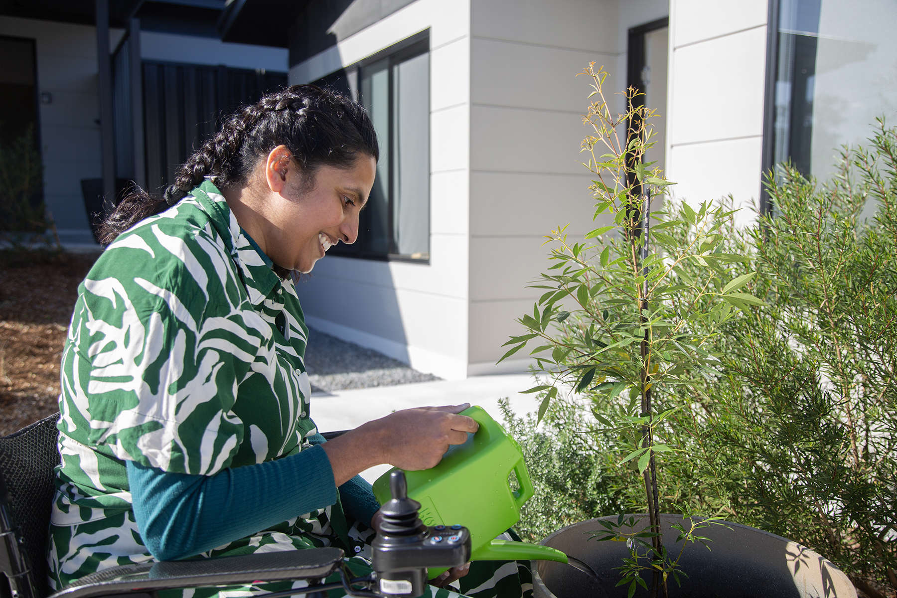 Vindya is watering some plants in her garden with a green watering can.