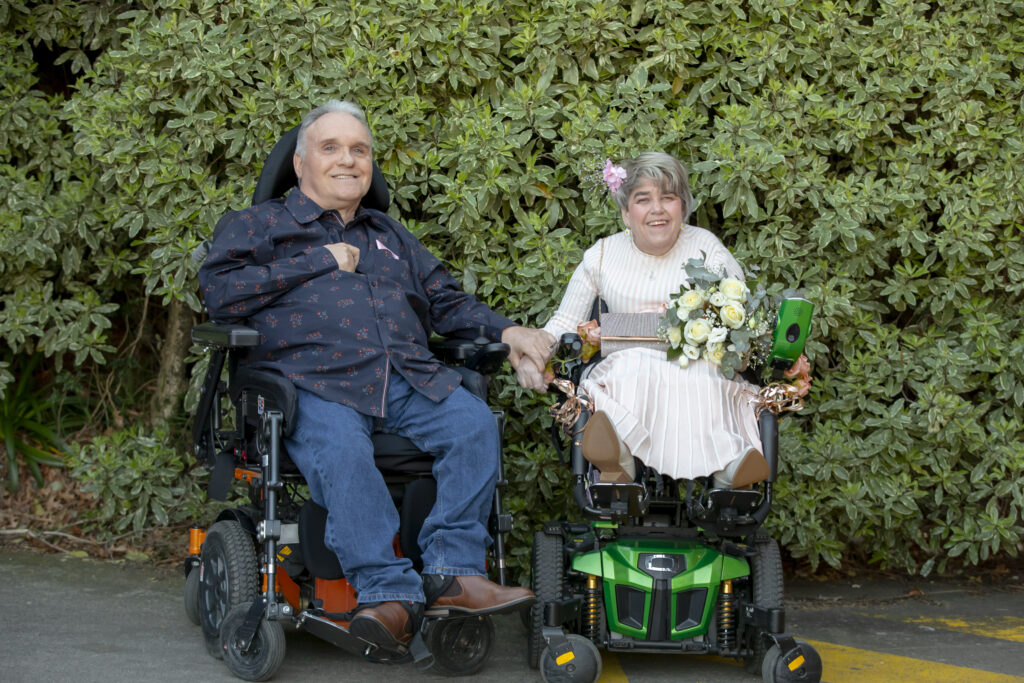 A man and a woman in a wheel chair holding hands
