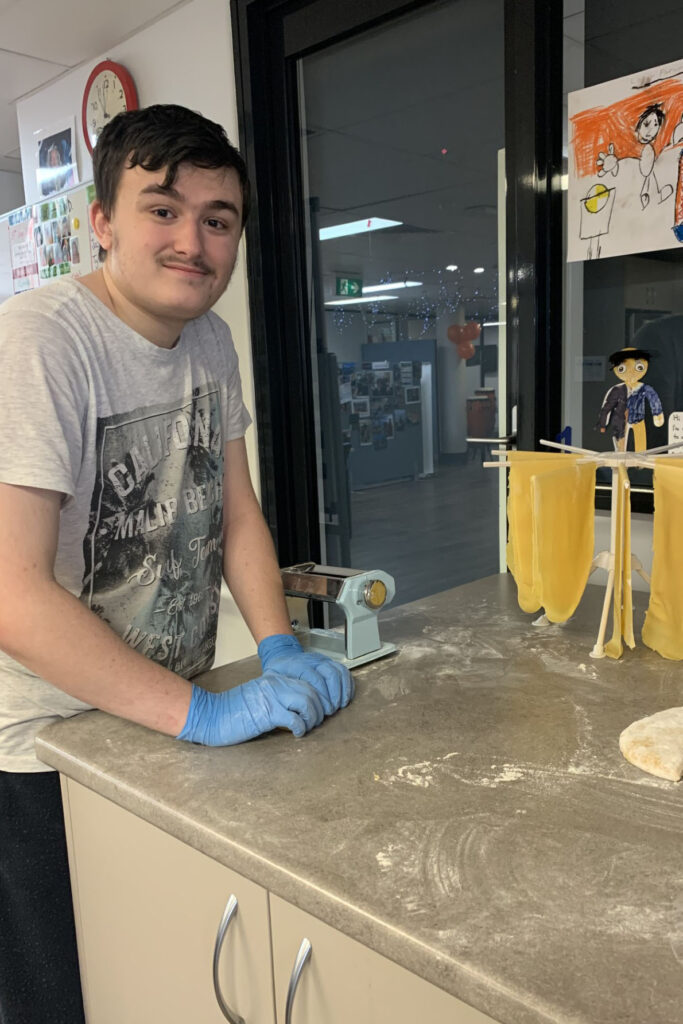 A young man is cutting fresh pasta - he is smiling