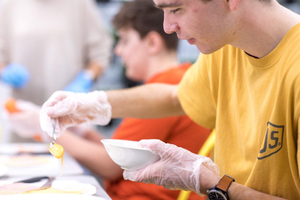 A young man is cooking in a kitchen - he has plastic gloves on.